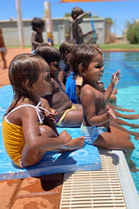 Aboriginal children sitting along the edge of a swimming pool