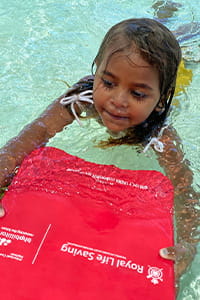 An Aboriginal girl swimming with a red Swim and Survive kickboard