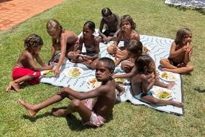Jigalong children eating lunch on the grass by the pool