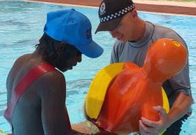 An aboriginal youth with a police officer in the pool attaching a rescue tube to a lifesaving manikin