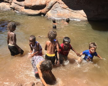Aboriginal children playing in a waterhole with red rocks behind them