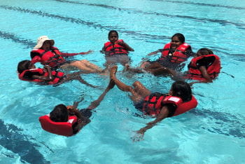 A group of aboriginal children int he water with their swim instructor, floating on their back while wearing lifejackets