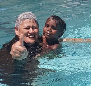 An adult and aboriginal child swimming together in the Jigalong pool