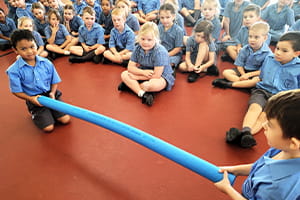 Primary students practising a reach rescue with a pool noodle
