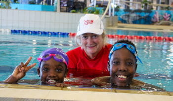 Two multicultural children with their Swim Instructor at the edge of the pool
