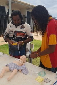 Pool Lifeguard Kimberley Rose French showing a parent how to conduct CPR on an infant manikin