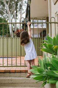 A little girl reaching up trying to open a pool gate