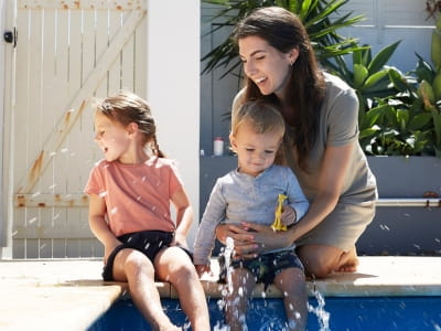 A mother and two young children play at the edge of the pool
