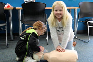 Two young girls practising CPR on a manikin