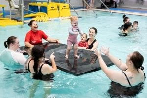 Infants enjoying a swimming lesson with their aprents and instructor