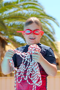 A child holding a rope and wearing red swimming goggles