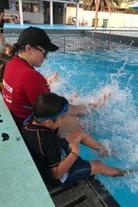 swimming instructor and students practising kicking at the edge of the pool