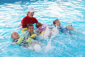 Children kicking on their back with pool noodles and their instructor