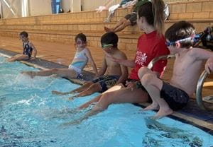 children and swim teacher sitting at edge of Leonora swimming pool