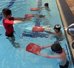 swimming instructor with students at edge of pool