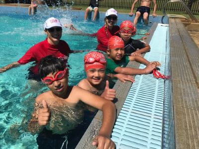 Two swim instructors in the water with multicultural children at Lynwood Senior High School