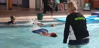 3 children in the water kicking on their back to their instructor at Bold Park