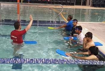 a swim instructor with 5 men in the water learning swimming skills