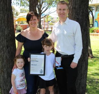 Sister Indy, Mum Kellie, Milla and Dad Dean standing with Milla's Bravery Award under a tree at Bateman Primary School