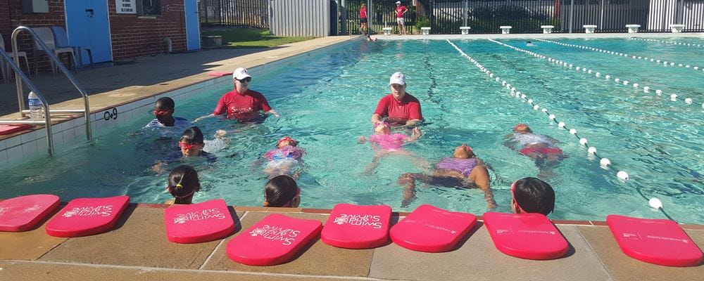 Two swimming instructors in the water with multicultural children doing a swimming lesson
