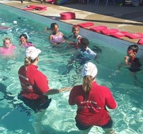 Two swimming instructors in the water with muticultural children doing a swimming lesson