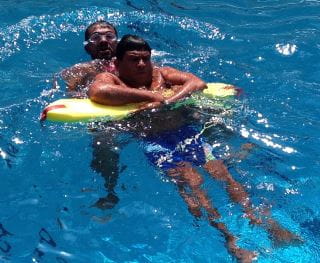 Two lifeguards in the pool in Oman practising rescues using a rescue tube