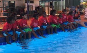 Aboriginal children sitting along the edge of the swimming pool at Newman Aquatic Centre
