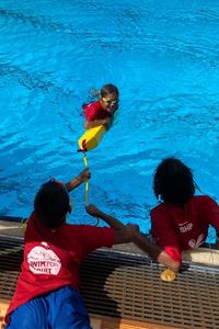 Two Aboriginal children rescuing their friend from a pool with a rescue tube