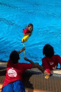 Two Aboriginal children rescuing their friend from a pool with a rescue tube