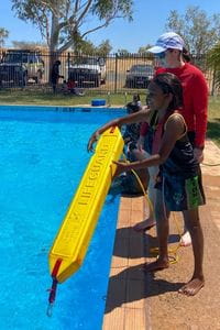 An Aboriginal children with a rescue tube standing on the edge of the pool with swim instructor Zoe Ross