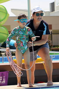 Child being helped to throw rope into pool