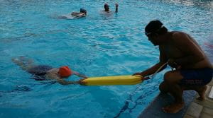 a lifeguard assisting a woman to the edge of the pool using a rescue tube
