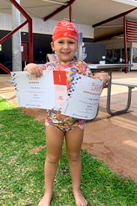 young girl wearing a swimming cap and holding up her swimming certificates