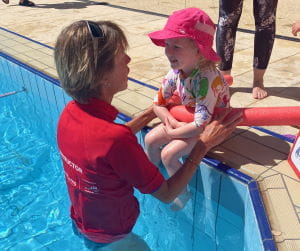 A swim instructor helping a toddler girl into the water