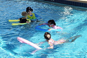 Three children in the pool with their instructor using noodles to float