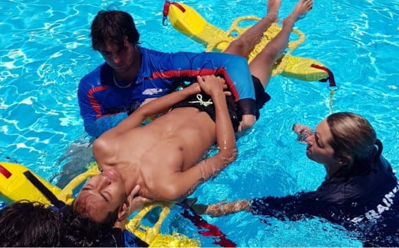 three people practising a spinal rescue in a swimming pool