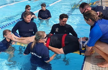 pool lifeguard trainers rehearsing a spinal injury rescue