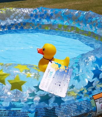 A rubber duck with the Don't Duck Out promotional message tied to it, sitting on the edge of a portable paddle pool
