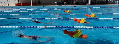 Children swimming in a pool towing orange manikins on rescue tubes