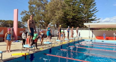 Kids and a parent lining up on the pool blocks for an obstacle relay