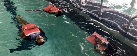 Three multicultural girls in the water floating on their backs with kickboards