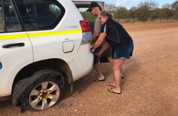 Tony Head from LIWA Aquatics and Jennifer Mickle from Royal Life Saving working together to repair a shredded tyre on their 4WD on a red dirt remote WA road