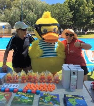 Two Rocjingham Aquatic centre staff members standing at a merchadise table with Dippy Duck mascot