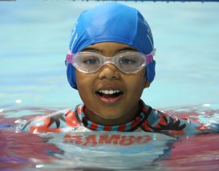 a child wearing goggles smiling at the camera while in the water
