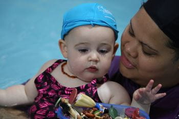 a baby with mummy in the water looking at toys