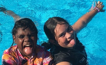 two Aboriginal girls in a swimming pool sticking their tongues out at the camera