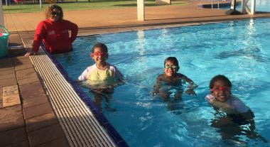 three children in pool with swim instructor