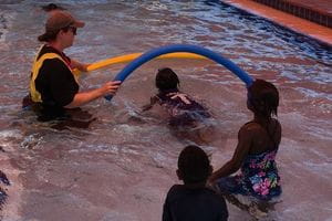 Aboriginal children in the pool with their instructor, swimming under a pool noodle arch
