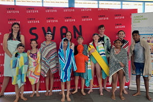 Group of young swimmers standing in front of Swan Active banner