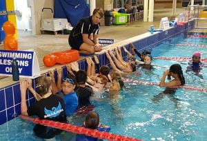 A lifeguard trainer on the edge of a pool with students in the water in front of him